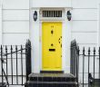 Porte d'entrée jaune vif avec escaliers et grille noirs