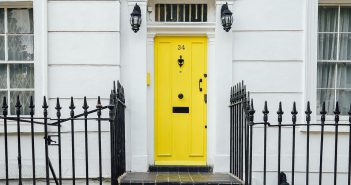 Porte d'entrée jaune vif avec escaliers et grille noirs